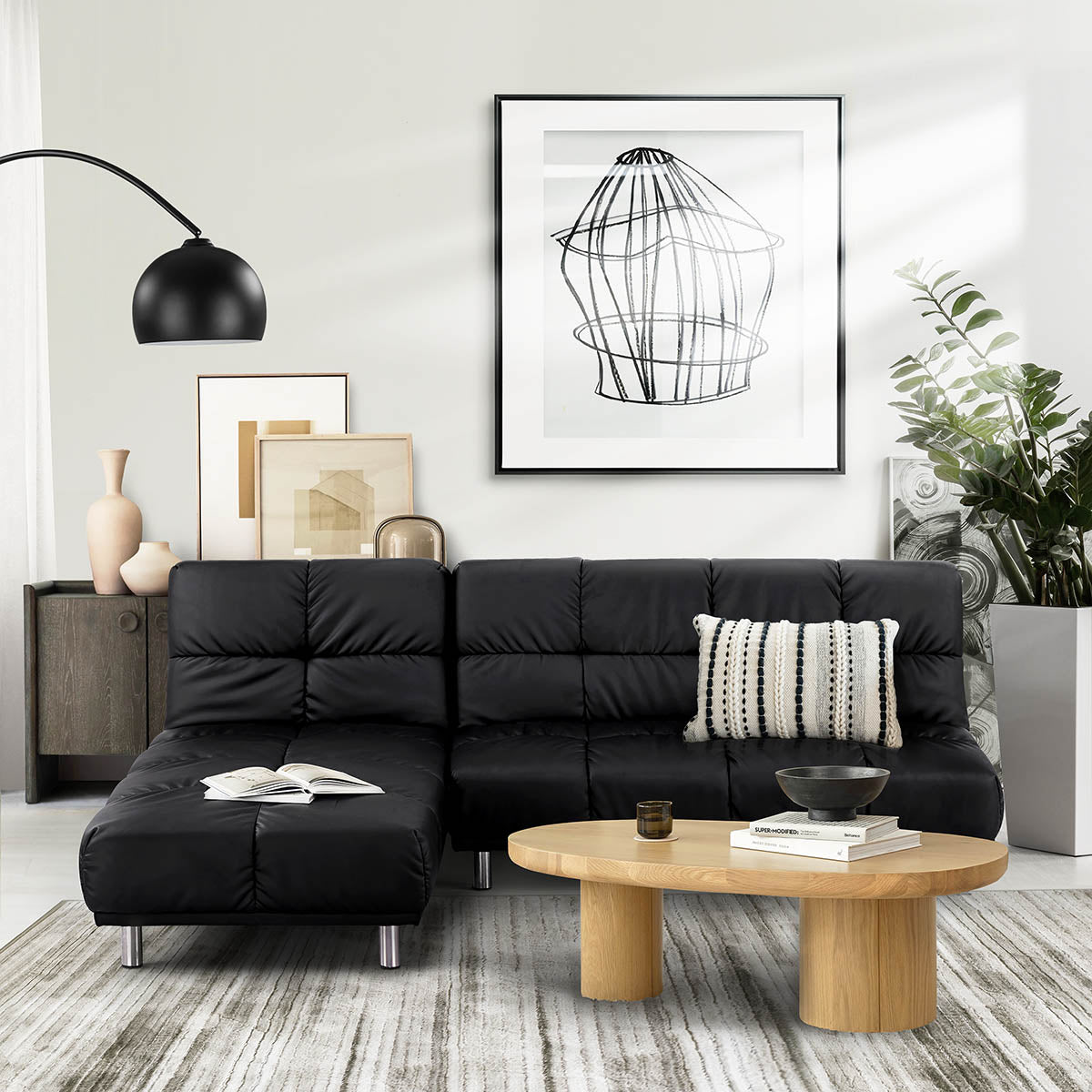 Canapé d’angle clic-clac en simili cuir noir dans un salon contemporain, avec méridienne réversible, coussin décoratif, table basse en bois clair et éléments décoratifs modernes, idéal pour un intérieur design et fonctionnel.